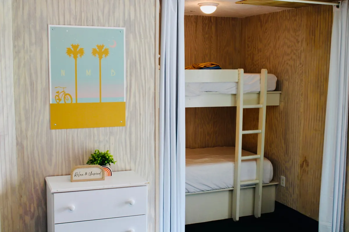 A cozy interior room featuring a set of bunk beds, whimsical decorative wall art, and a dresser topped with a potted plant. The scene conveys a welcoming atmosphere, ideal for families or groups enjoying a relaxing stay together. Soft lighting and thoughtful touches throughout the room reinforce a sense of comfort and togetherness.