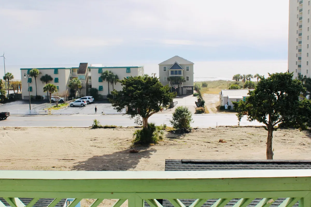 The image showcases a serene ocean view framed by two swaying trees, with colorful beachside buildings nearby. The scene captures a peaceful sunrise over the water, inviting morning walks on the sand and hinting at the vibrant community atmosphere just steps away.
